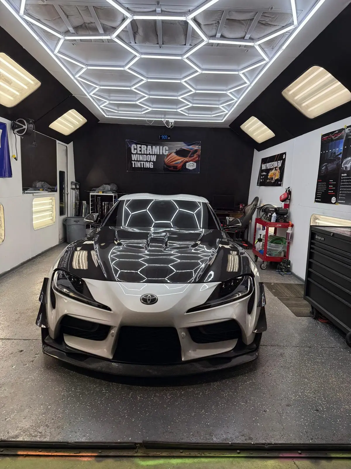A Toyota Supra in the shop with a hexagon window tint pattern across the glass